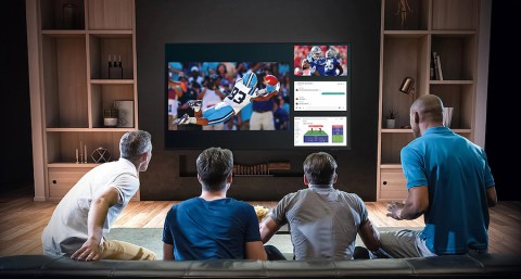  Friends gathered on a couch watching a football game on a large home theater screen.